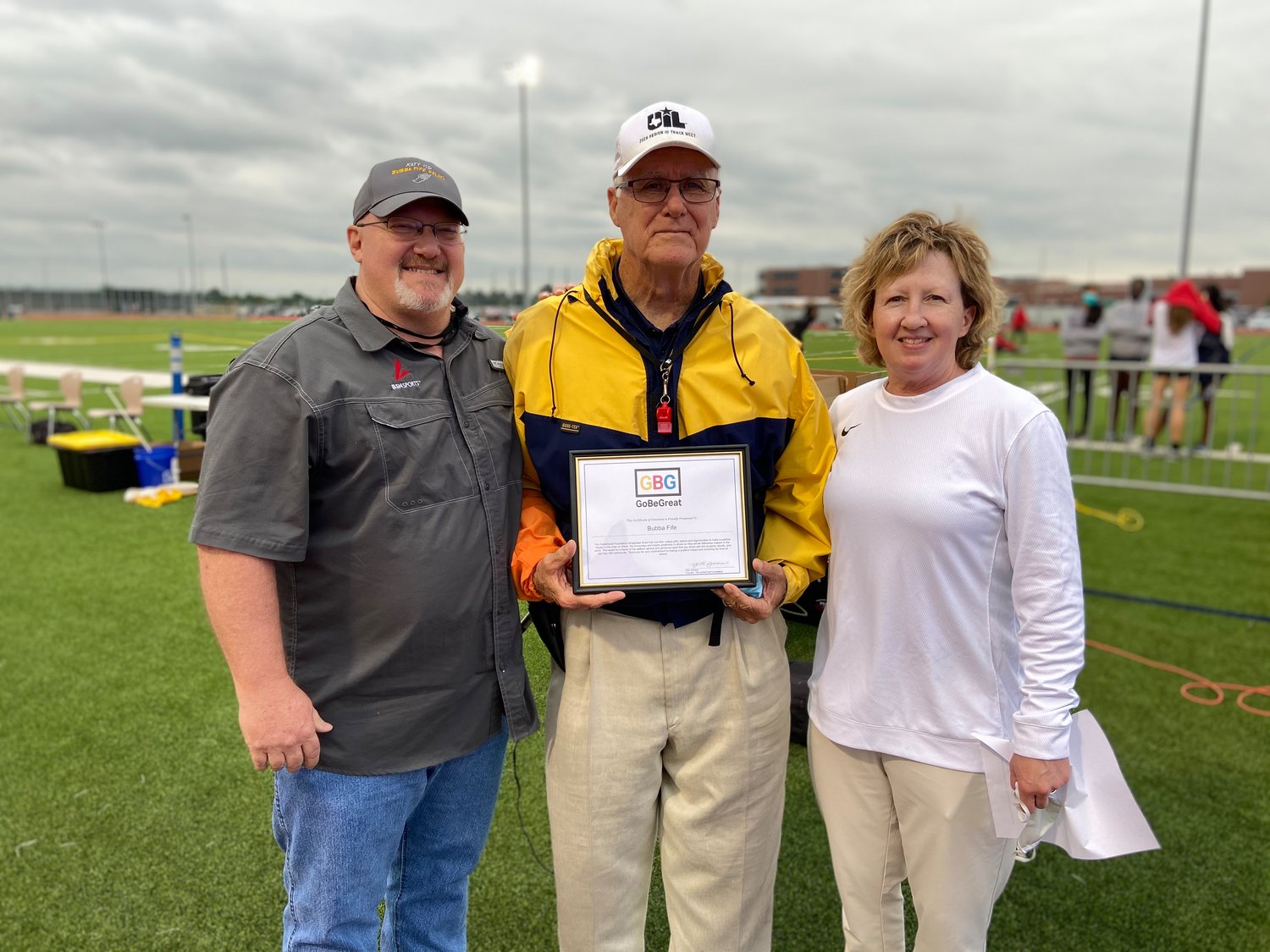 Longtime Katy ISD coach Bubba Fife, middle, is pictured with Katy ISD athletic director Debbie Decker (right) and a representative from BSN Sports. Fife was recognized with the Be Great award on April 15 prior to the second day of the 19-20-6A area track and field meet at Paetow High. The award honors those who serve with kindness and selflessness.